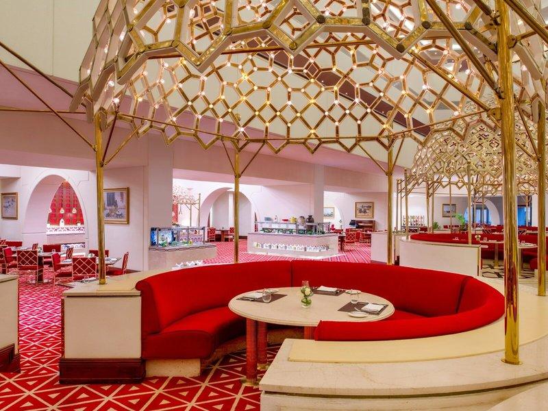 Innenbereich des Sheraton Doha Resort Convention Hotel mit goldenen, netzartigen Strukturen und roten Sitzgelegenheiten.