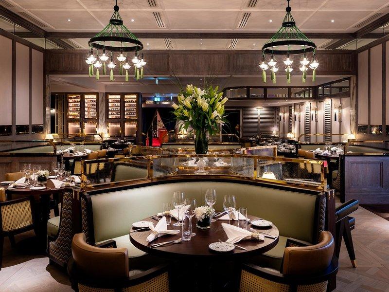 Innenansicht des Restaurants im Sheraton Doha Resort Convention Hotel mit gerahmten Sitzbänken, Tischdecken und Weinflaschen.