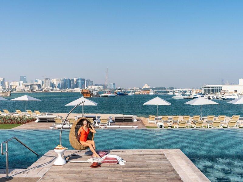Frau in einem Korbsessel am Pool des Rixos Gulf Hotel Doha mit Blick auf die Stadt