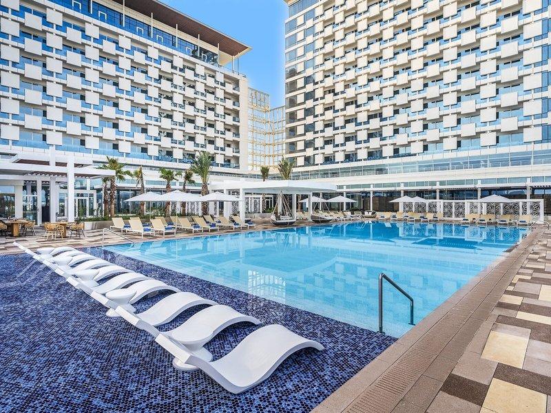 Außenpoolbereich des Rixos Gulf Hotel Doha mit Loungestühlen und Sonnenschirmen.