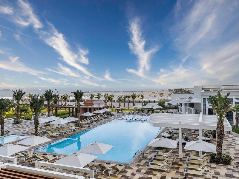 Aussicht auf den Poolbereich des Rixos Gulf Hotel Doha mit Loungeliegen und Sonnenschirmen