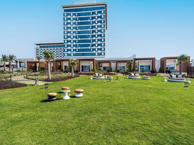 Außenbereich des Rixos Gulf Hotel Doha mit Rasen, Möbeln und hohen Gebäuden