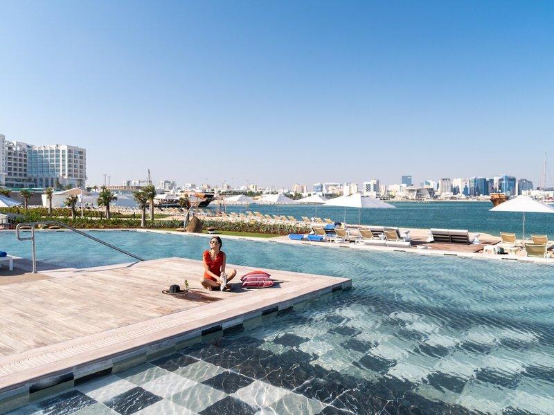 Ein Gast sitzt am Rand des Pools im Rixos Gulf Hotel Doha mit Blick auf die Stadt.