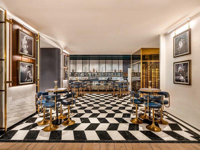Innenbereich der Bar im Rixos Gulf Hotel Doha mit schwarzen und weißen Schachbrettboden und goldenen Stühlen.