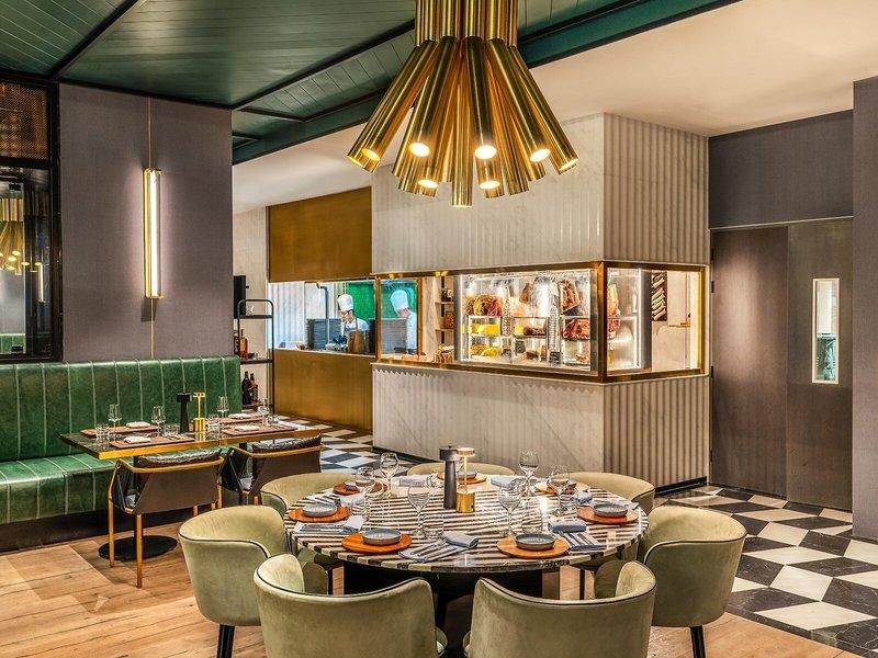 Innenbereich des Rixos Gulf Hotel Doha mit modernem Restaurant, grünen Sesseln und zentralem Tisch.