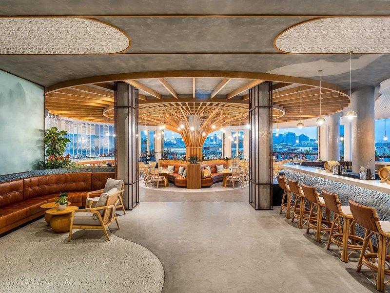 Innenansicht der Lounge im Rixos Gulf Hotel Doha mit Holzmöbeln und Panoramafenstern.