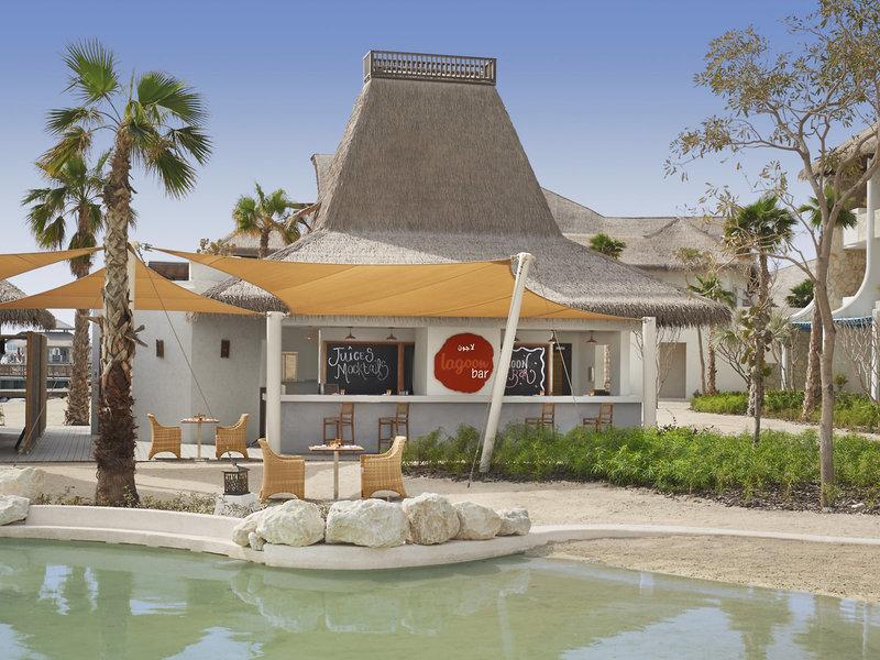 Außenansicht der Pool-Bar im Banana Island Resort Doha von Anantara mit Palmen und einem Pool davor.