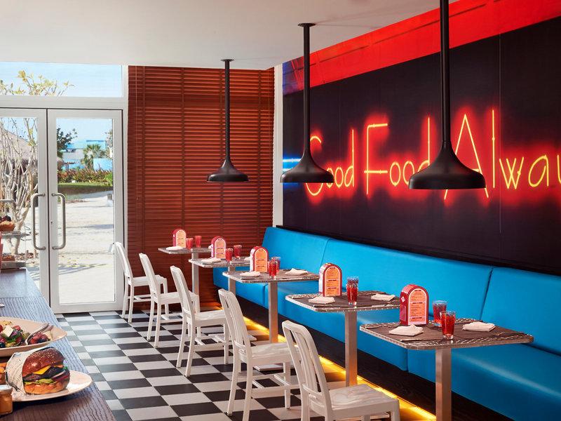 Interieur von Banana Island Resort Doha by Anantara mit Esstischen, neon Schriftzug 'Good Food Always' und roten Neonbeleuchtung.
