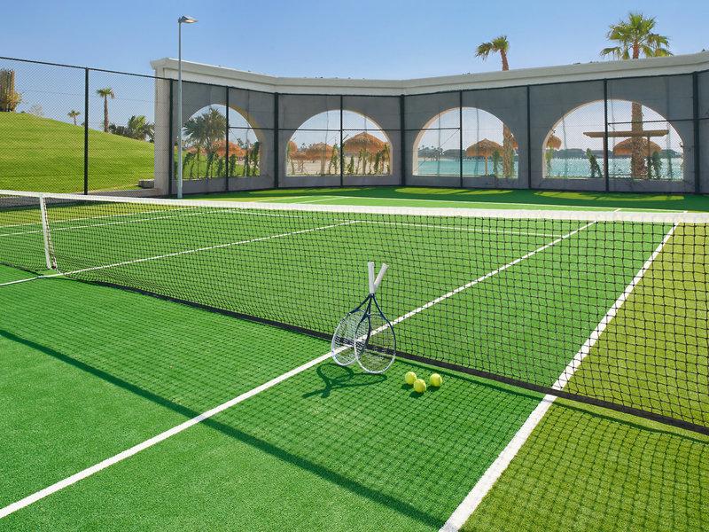 Tennisplatz im Banana Island Resort Doha von Anantara mit Schlägern und Tennisbällen auf dem grünen Platz.