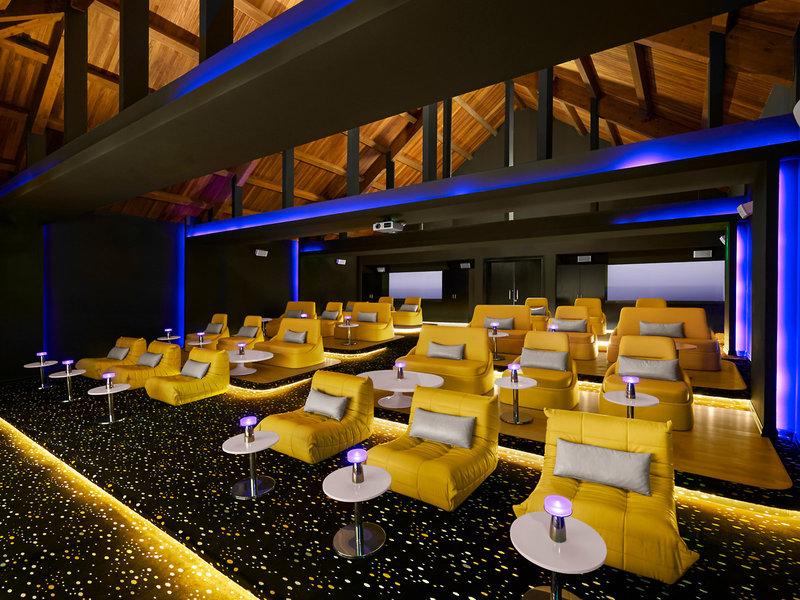 Kinosaal im Banana Island Resort Doha von Anantara mit gelben Sesseln und blauer Beleuchtung.