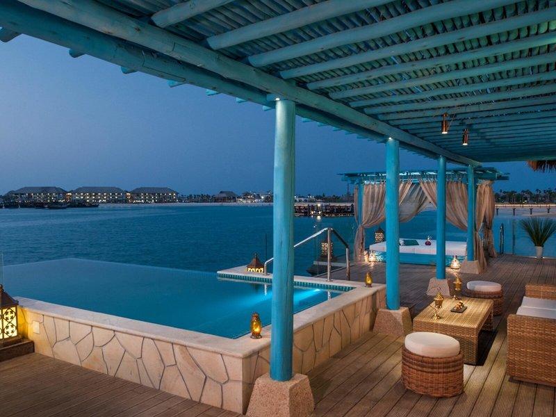 Poolbereich des Banana Island Resort Doha von Anantara bei Nacht mit Überdachung, Sitzmöbeln und Blick aufs Meer.