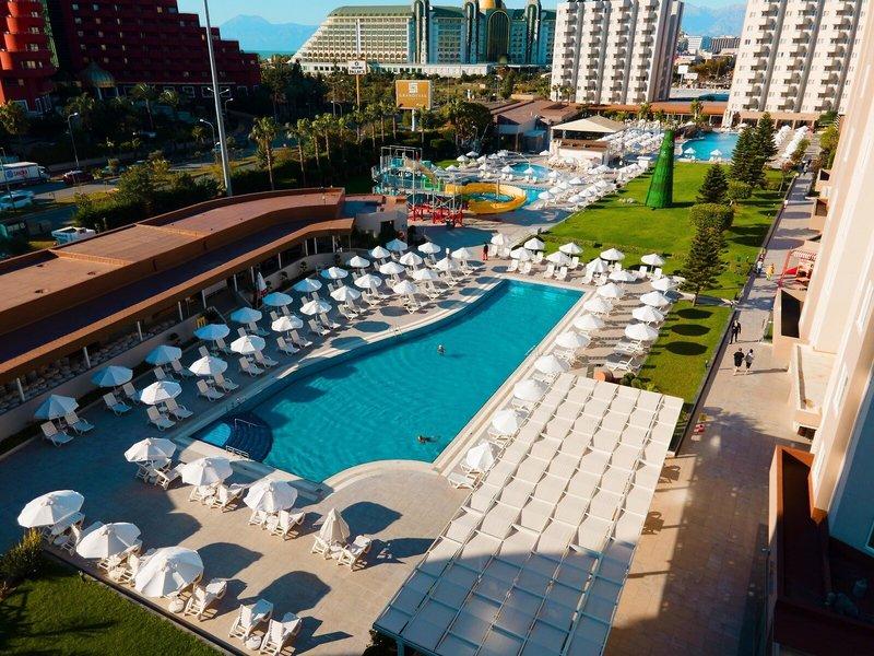 Außenansicht des Grand Park Lara Hotels mit Poolbereich, Liegestühlen und Wasserrutsche.