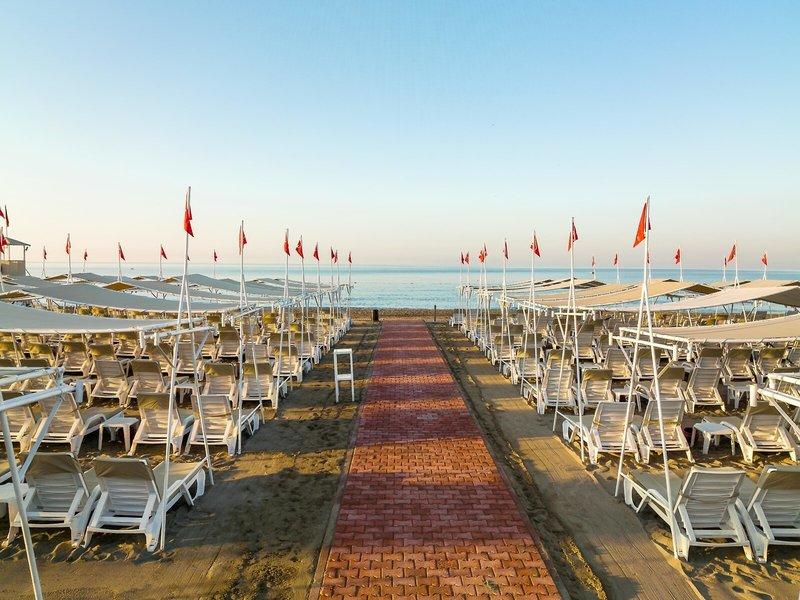 Strand des Grand Park Lara Hotels mit vielen weißen Sonnenliegen und roten Fahnen