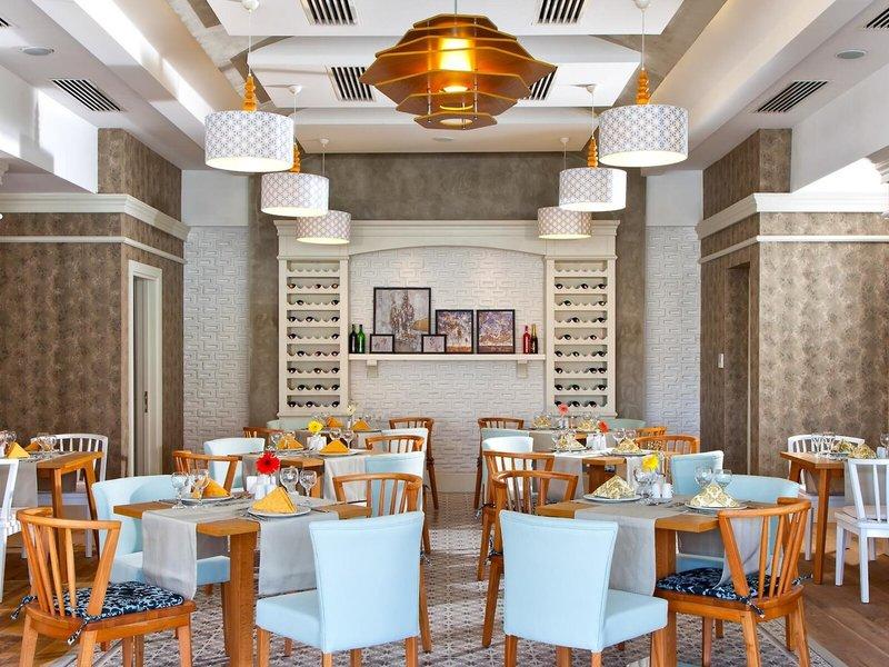 Innenbereich des Grand Park Lara Hotels mit geometrischen Mustern, blauen Stühlen und Tischen, beleuchteten Kronleuchtern und einer weißen Wand mit Weinregalen.