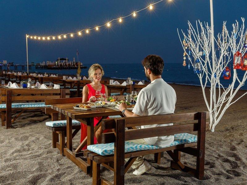Paar isst am Tisch auf dem Strand des Grand Park Lara Hotels bei Nacht.