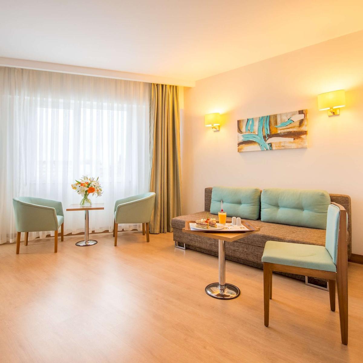 Hotelzimmer mit Sofa, Tisch, Blumen und Kissen.