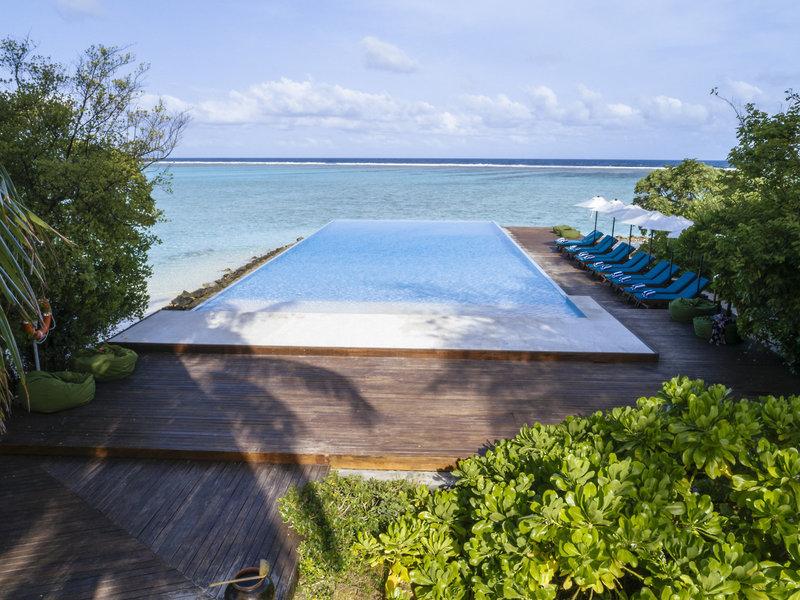 Infinity-Pool am Strand des Summer Island Maldives Hotels mit blauen Sonnenliegen und grünen Kissen.