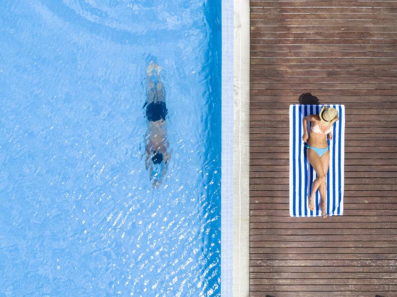 Blick von oben auf einen Pool im Hotel Summer Island Maldives mit einer Person, die schwimmt und einer anderen, die auf einem Handtuch liegt.