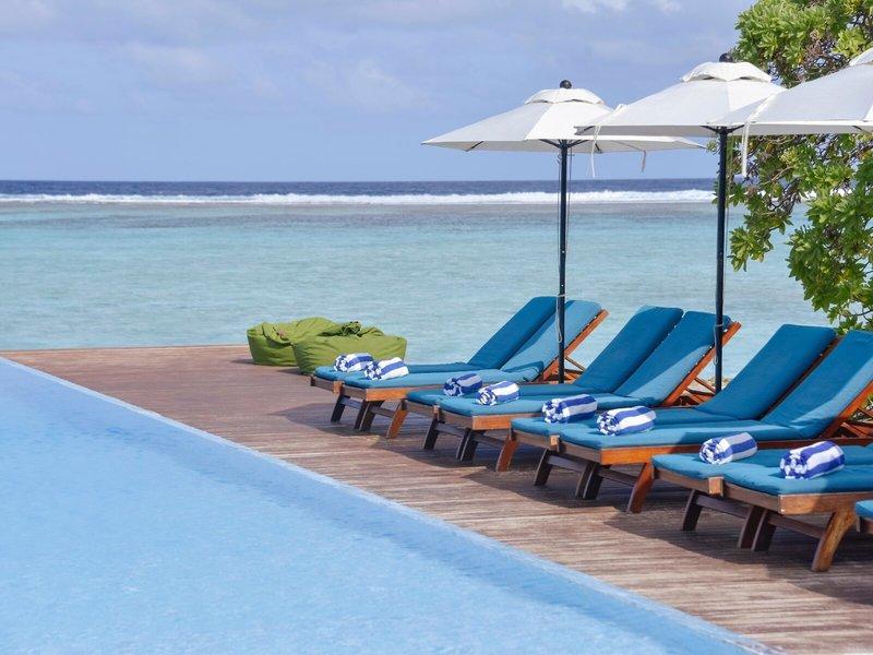 Am Pool der Summer Island Maldives stehen blaue Lounge-Stühle mit weißen Sonnenschirmen.
