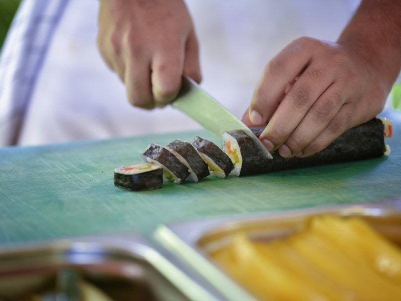 Person schneidet Sushi auf einem grünen Schneidebrett im Hotel Summer Island Maldives.