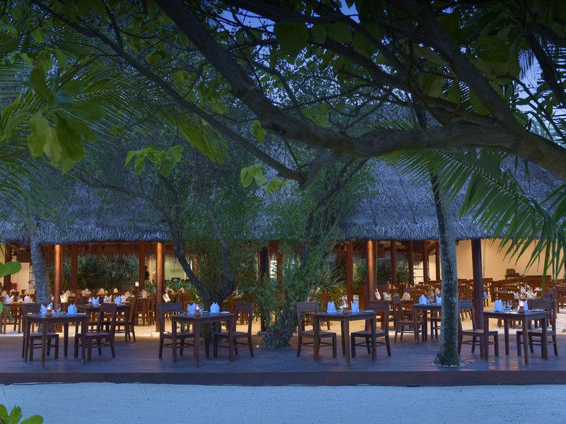 Außenbereich des Restaurants im Summer Island Maldives Hotel mit gedeckten Tischen und tropischen Bäumen.