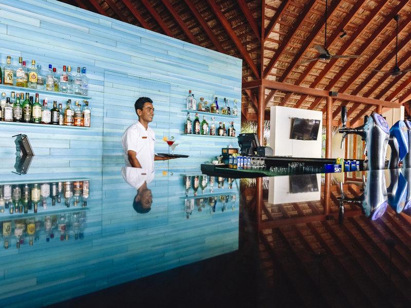Ein Barkeeper im Summer Island Maldives Hotel serviert ein Getränk an der Theke.