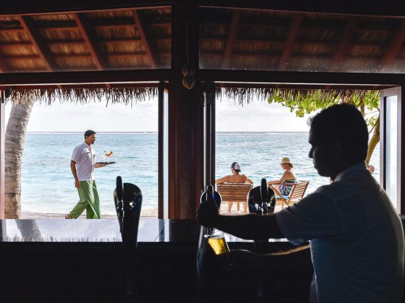 Mitarbeiter serviert Getränke an der Bar im Summer Island Maldives Hotel mit Blick auf den Strand und das Meer.