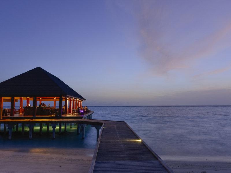 Hotelterrasse des Summer Island Maldives bei Sonnenuntergang, mit leuchtenden Lichtern und Blick aufs Meer.