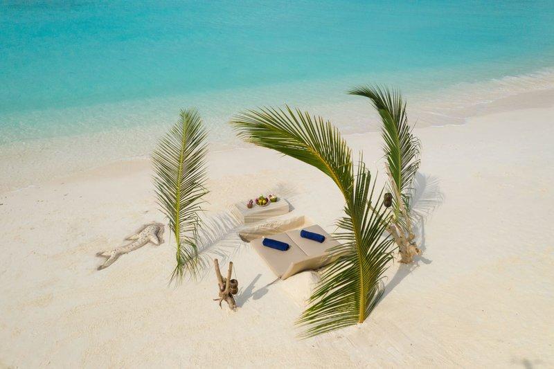 Strandlounge im Brennia Kottefaru Maldives mit weißen Liegen und Palmen