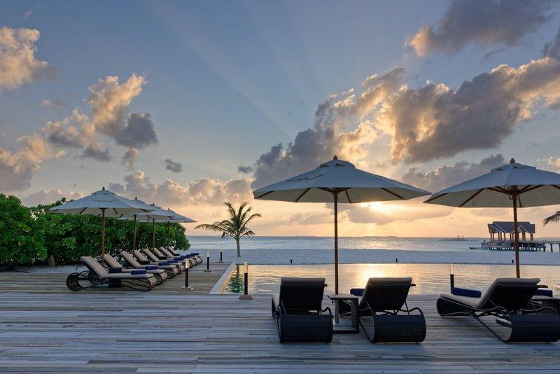 Sonnenuntergang am Strand des Brennia Kottefaru Maldives Hotels mit Liegen und Sonnenschirmen.