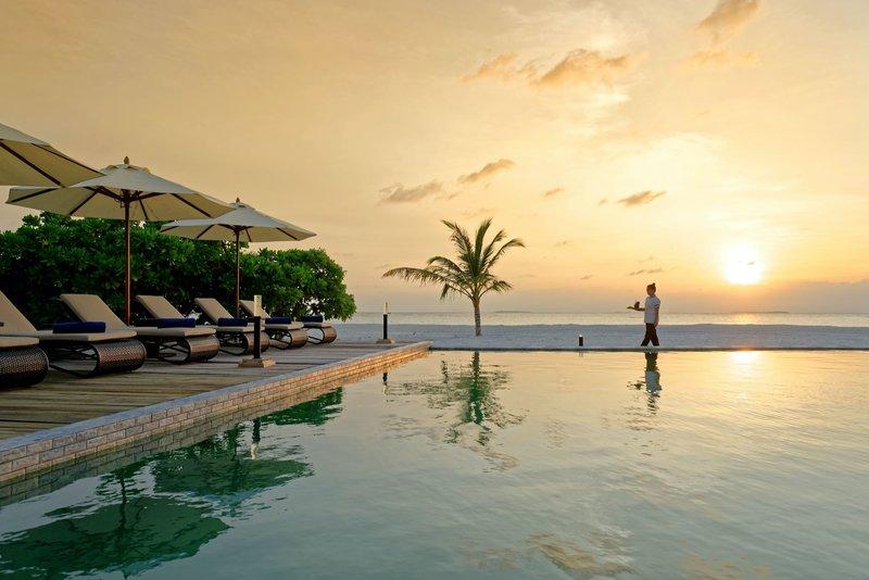 Ein Pool am Strand bei Sonnenuntergang mit Sonnenschirmen und Liegen im Brennia Kottefaru Maldives.