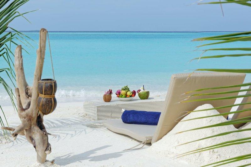 Ein Strand mit Liegen, Früchten und einer Kokosnuss an einem ruhigen Tag.