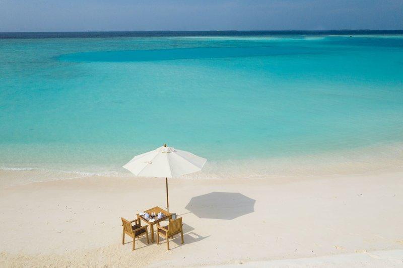 Ein Tisch mit einem Schirm auf dem Strand des Brennia Kottefaru Maldives.