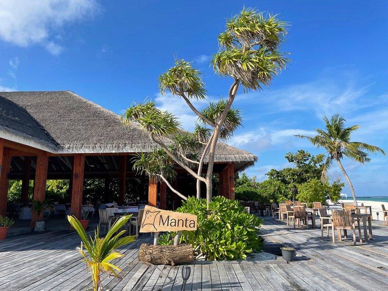 Foto der Außenterrasse des Brennia Kottefaru Maldives Hotels mit Holzboden, Tischen, Stühlen und Palmen.