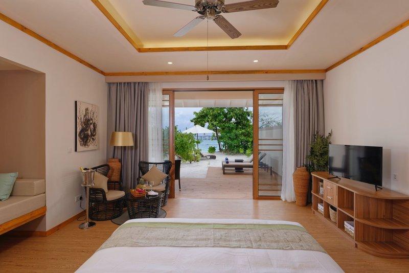 Innenansicht des Schlafzimmers im Brenneri Kottefaru Maldives mit offenem Fenster, Blick auf den Strand und modernen Möbeln.