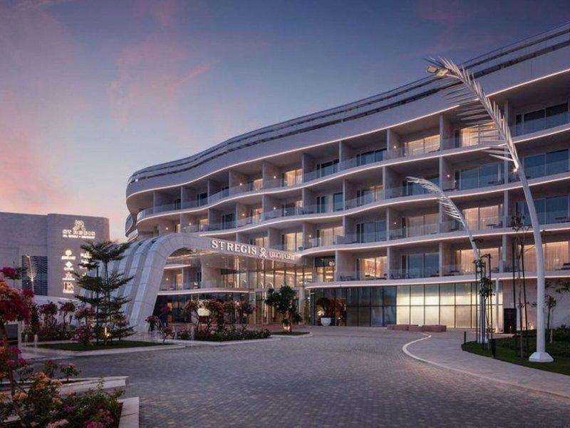 Außenansicht des St. Regis Al Mouj Muscat Resorts bei Nacht mit Beleuchtung und gepflanzten Gärten davor.