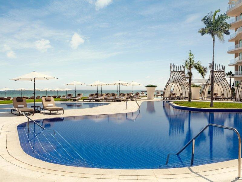 Außenpoolbereich des St. Regis Al Mouj Muscat Resorts mit Sonnenliegen und Sonnenschirmen.