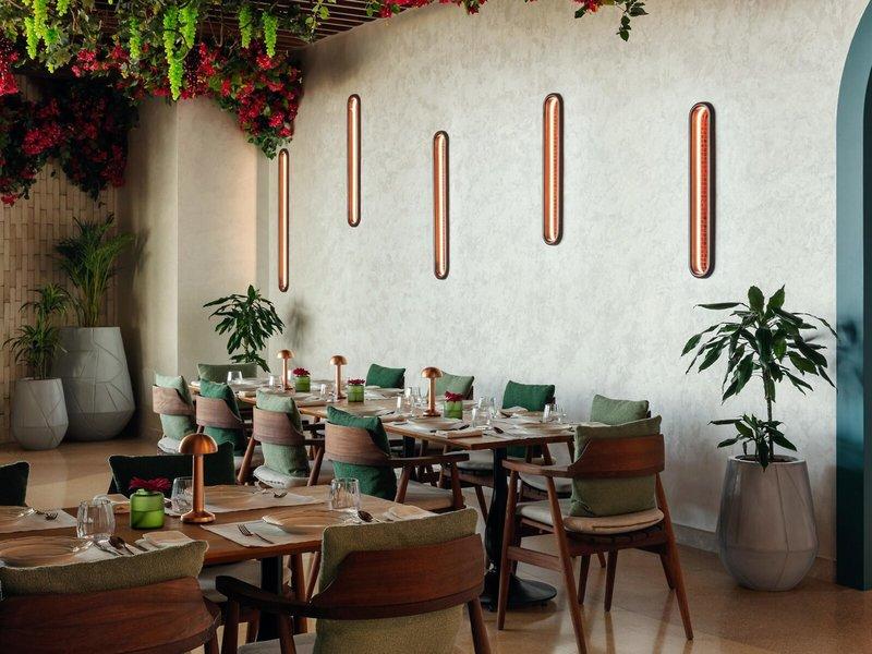 Restaurantbereich im St. Regis Al Mouj Muscat Resort mit Tisch, Stühlen, Pflanzen und Wandleuchten.