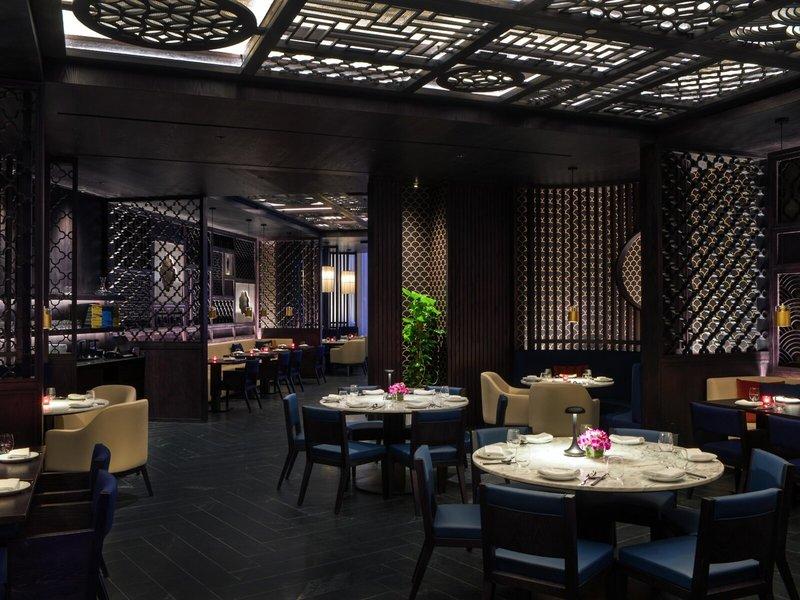 Innenansicht des Restaurants im St. Regis Al Mouj Muscat Resort mit dunklen Möbeln und goldenen Akzenten.