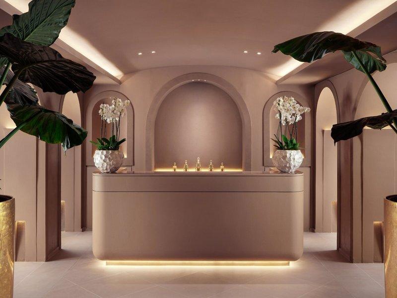 Empfangsbereich des St. Regis Al Mouj Muscat Resorts mit einer Theke, Blumenvasen und Beleuchtung.