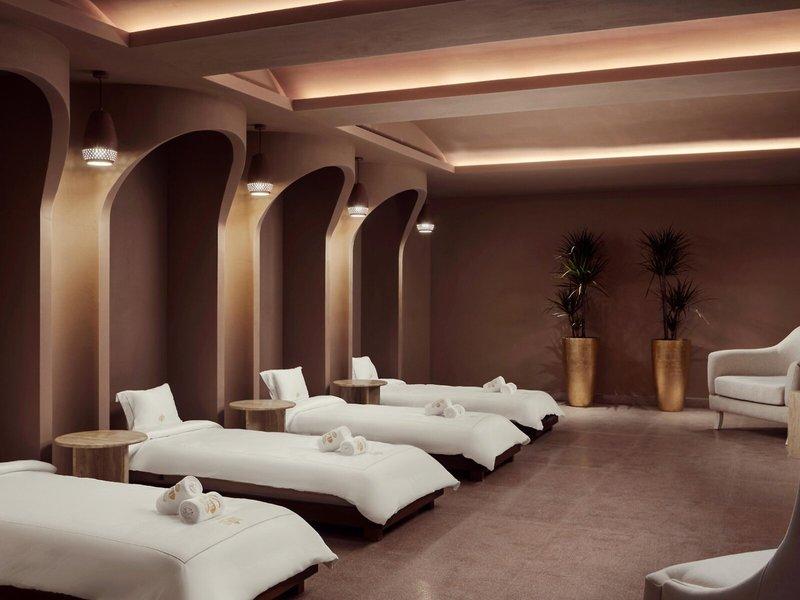 Spa-Behandlungsraum im St. Regis Al Mouj Muscat Resort mit mehreren weißen Liegen und goldenen Vasen.