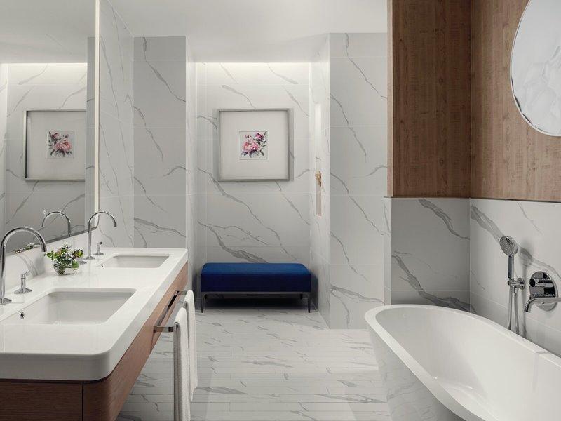 Das Badezimmer im St. Regis Al Mouj Muscat Resort mit weißen Marmorfliesen, einem blauen Hocker, zwei Waschbecken und einer Badewanne.