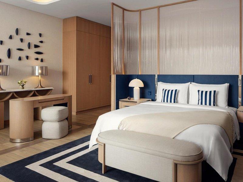 Inneneinrichtung eines Schlafzimmers im St. Regis Al Mouj Muscat Resort mit einem großen Bett, Nachttischen, Lampen und einem Schreibtisch.