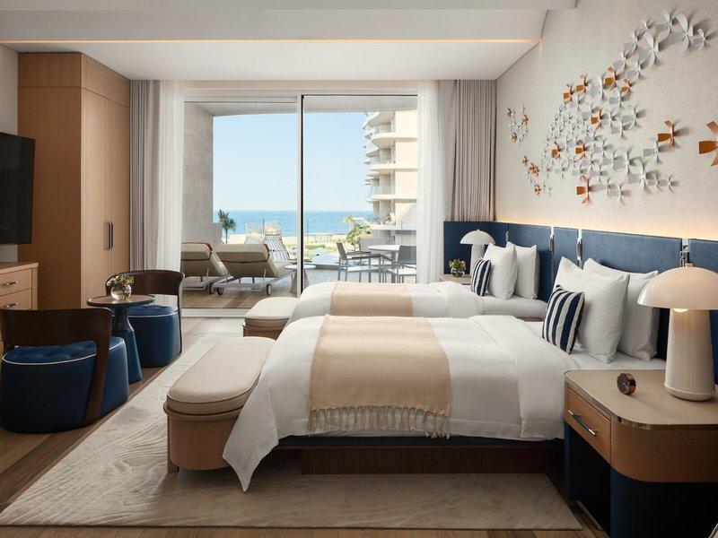 Schlafzimmer im St. Regis Al Mouj Muscat Resort mit Meerblick und zwei Betten.