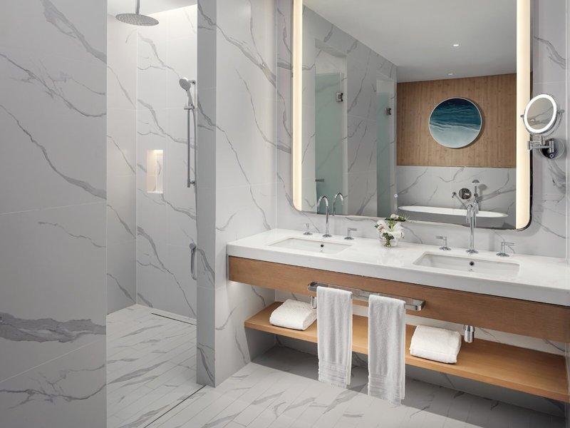Das Badezimmer des St. Regis Al Mouj Muscat Resort mit weißen Marmorwänden und einem großen Spiegel.