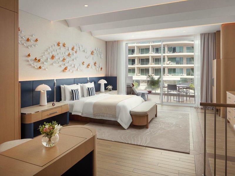 Innenansicht eines Zimmers im St. Regis Al Mouj Muscat Resort mit Bett, Nachttischen und Balkon.