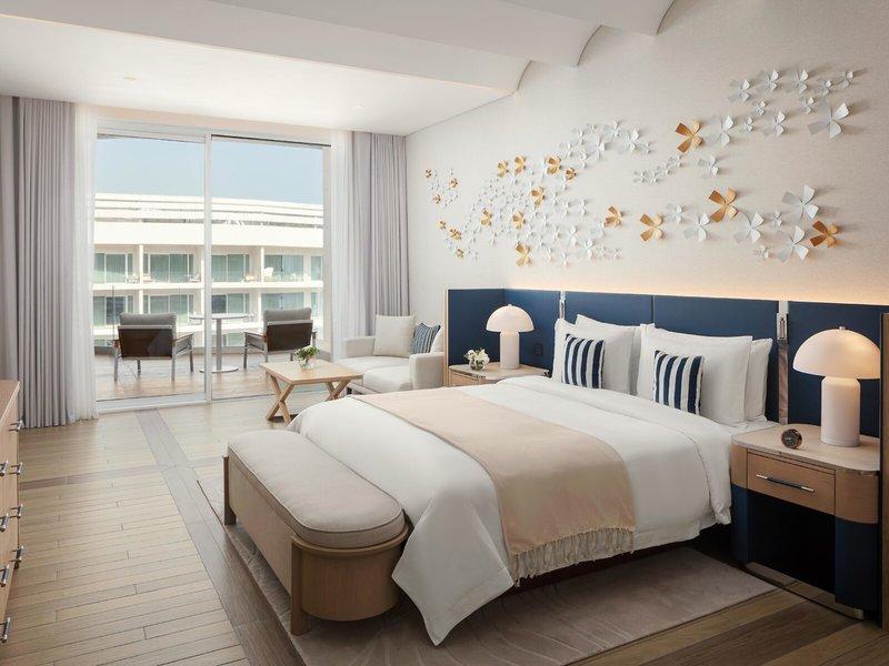 Schlafzimmer im St. Regis Al Mouj Muscat Resort mit großem Bett, Wanddekorationen und Blick auf Außenterrasse.
