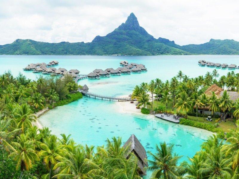 Aussicht auf das InterContinental Bora Bora Resort und Thalasso Spa mit blauem Wasser, Überwasser-Bungalows und Bergen im Hintergrund.