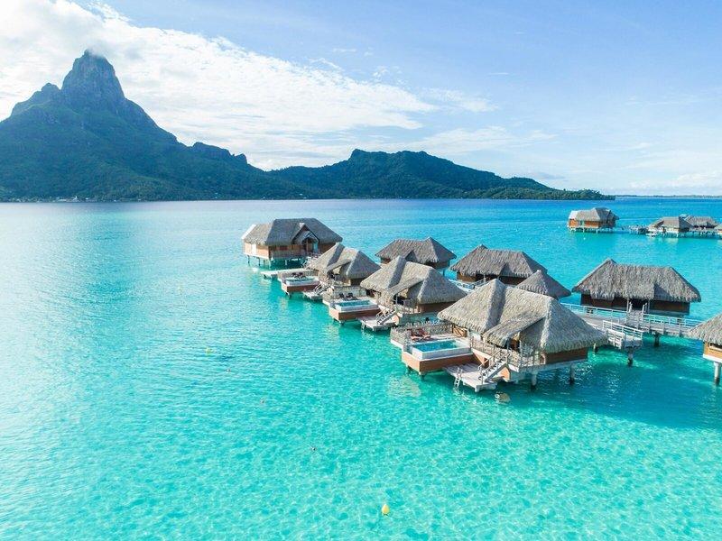 Luftaufnahme des InterContinental Bora Bora Resorts und Thalasso Spa mit Wasservillen vor einer bergigen Kulisse.