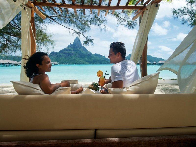 Ein Paar im InterContinental Bora Bora Resort genießt einen Drink unter einem Baldachin am Strand.